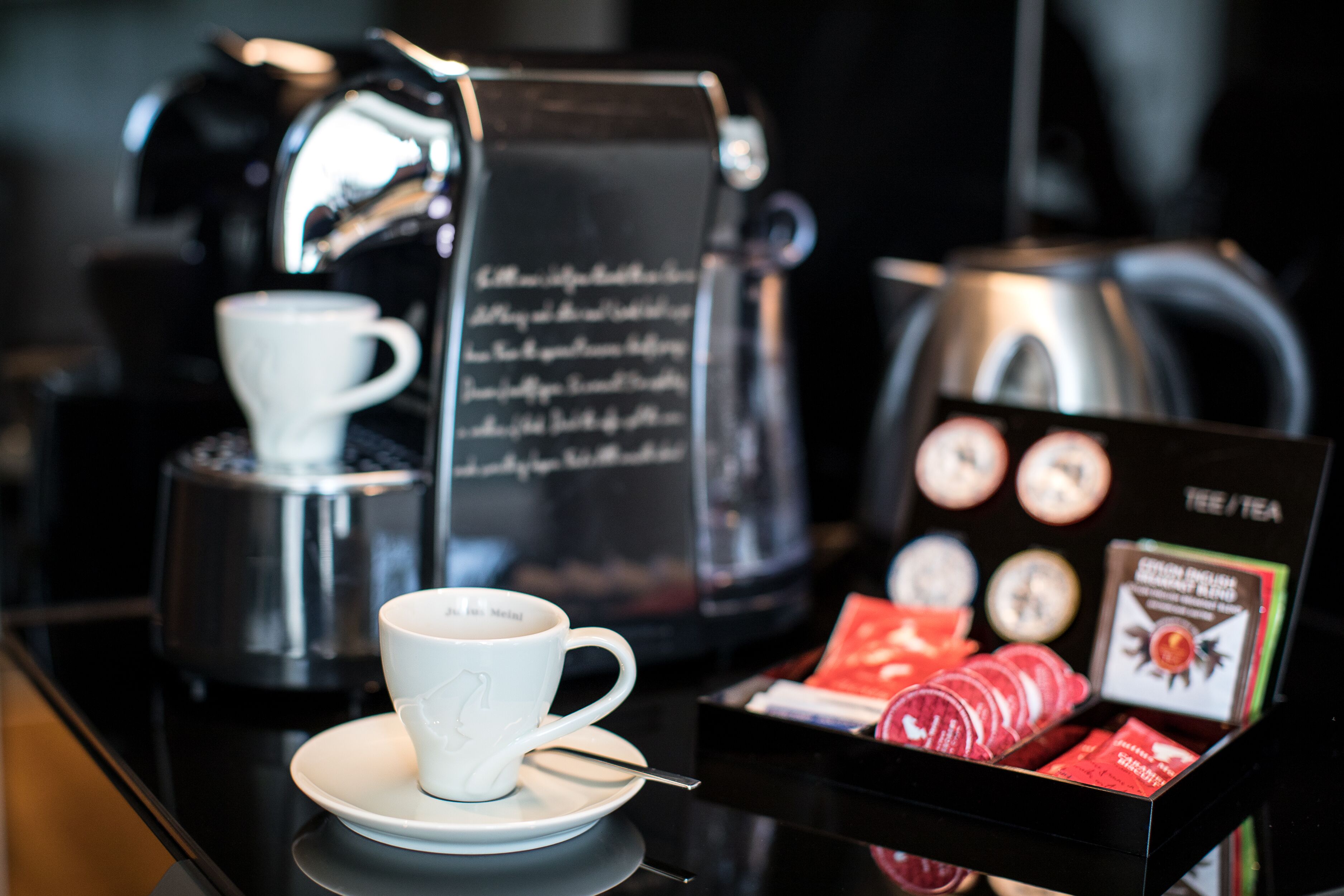 A coffee station with a cup, a spoon, and a tray of red coffee capsules.