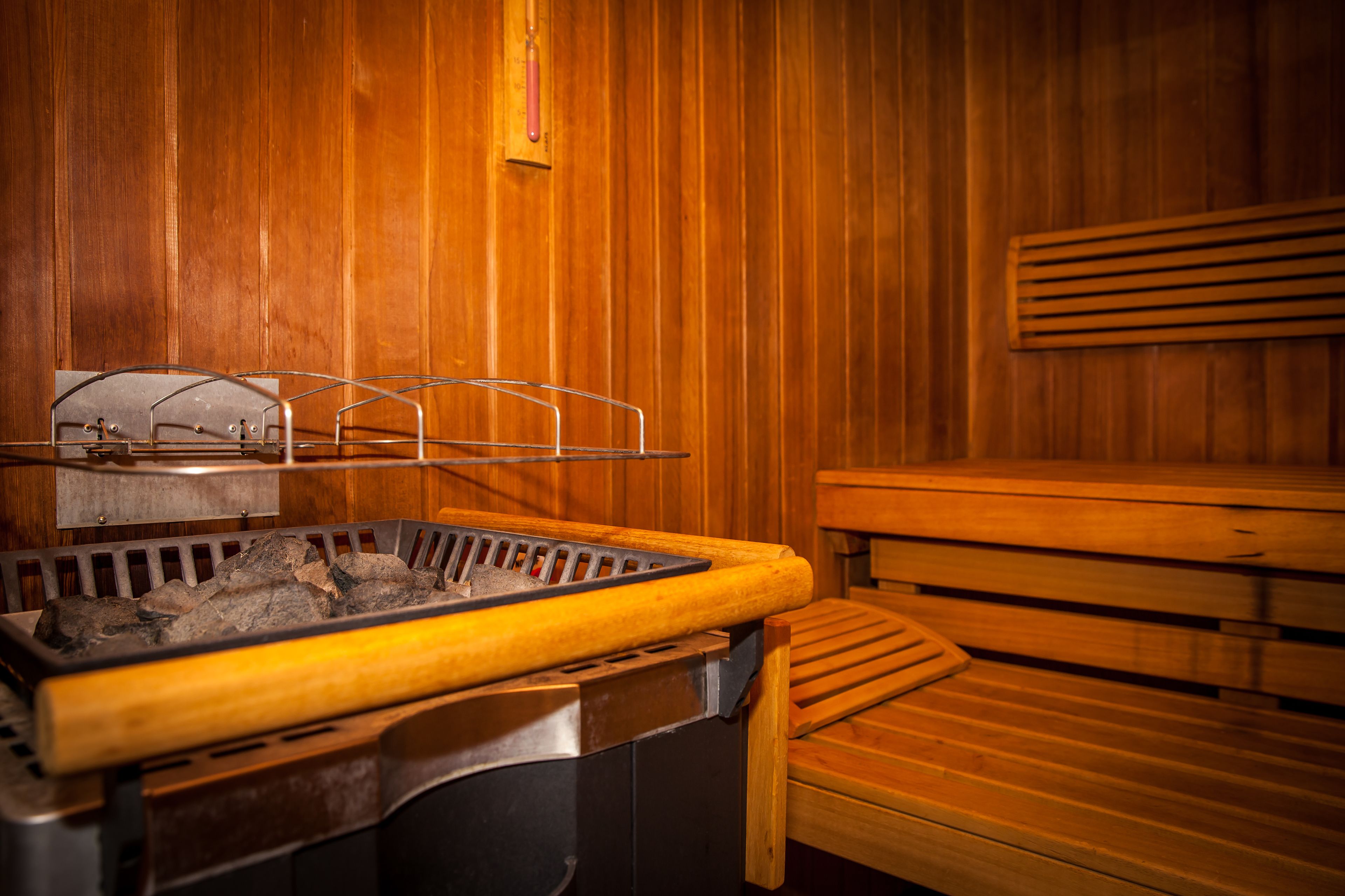 A sauna with a wooden bench, a metal bench, and a heating element with rocks.