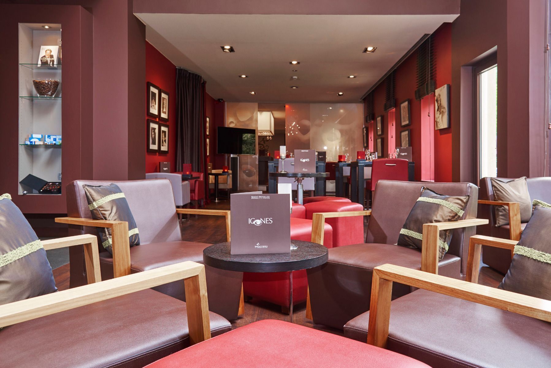 A modern lounge area with leather sofas, wooden tables, and a red accent wall.