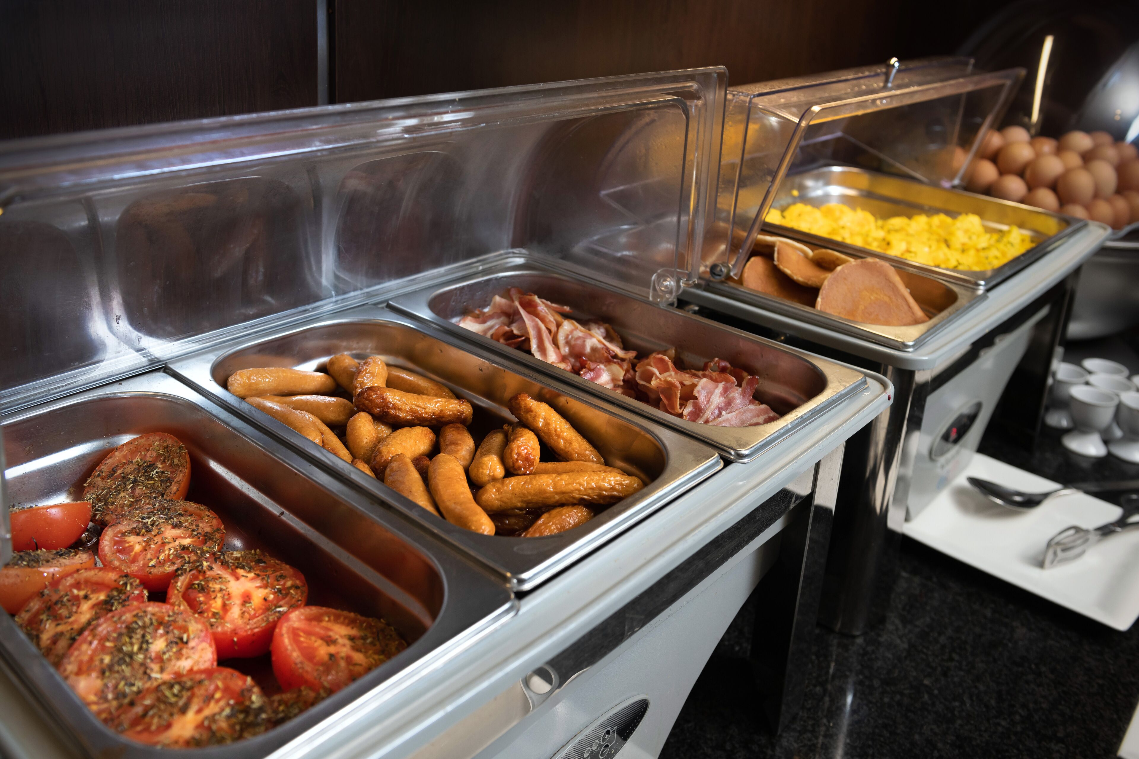 A buffet with various food items including tomatoes, sausages, eggs, and ham.