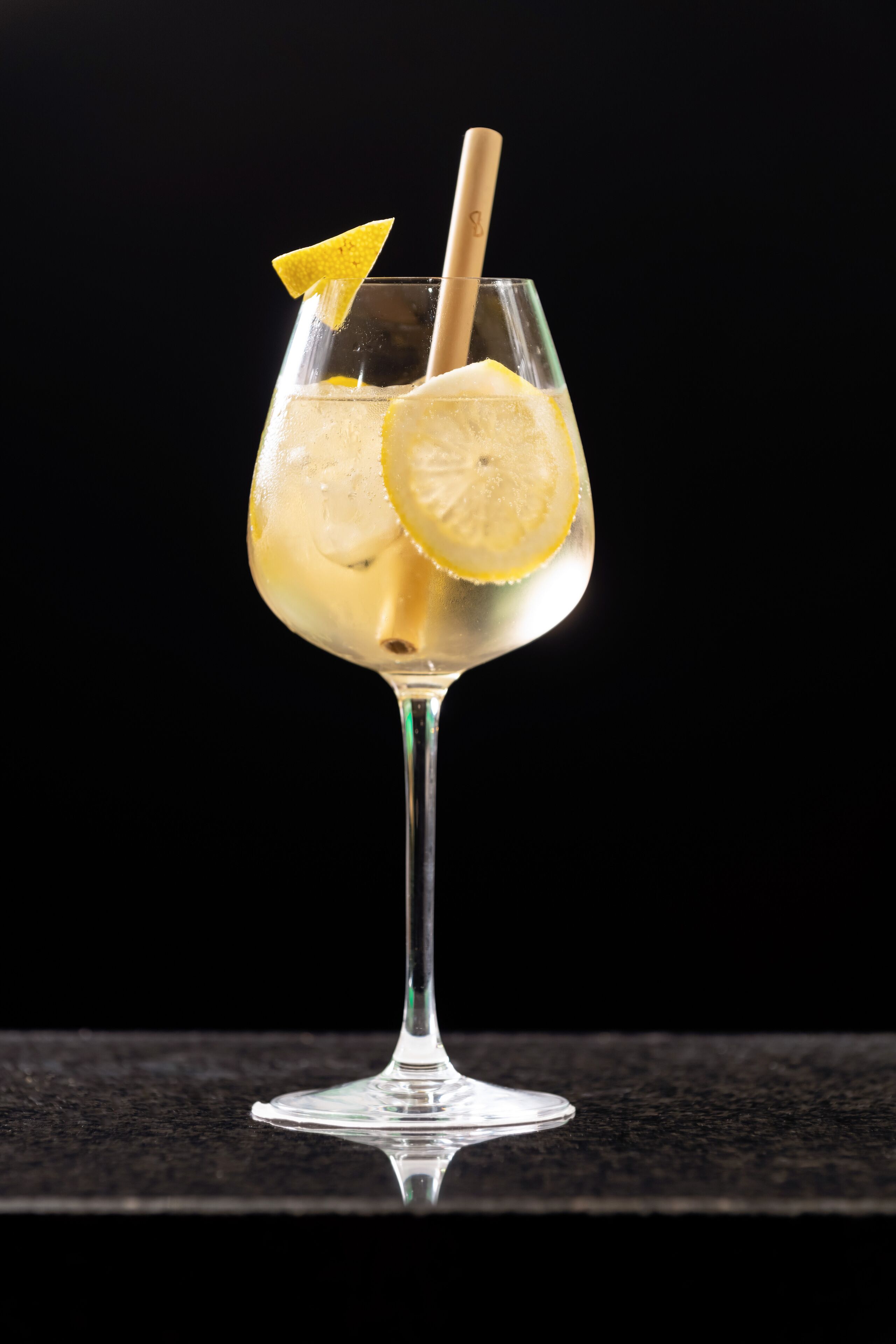 Un verre contenant une boisson claire, une tranche de citron et une paille, le tout présenté sur un fond sombre.