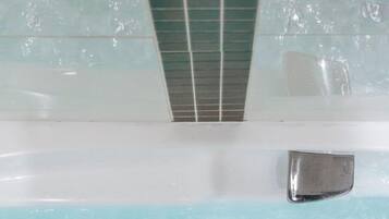 Une baignoire remplie d’eau claire, un mur recouvert de carreaux et une poignée en métal.