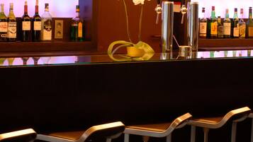 A bar area with multiple liquor bottles, a vase with flowers, and bar stools.