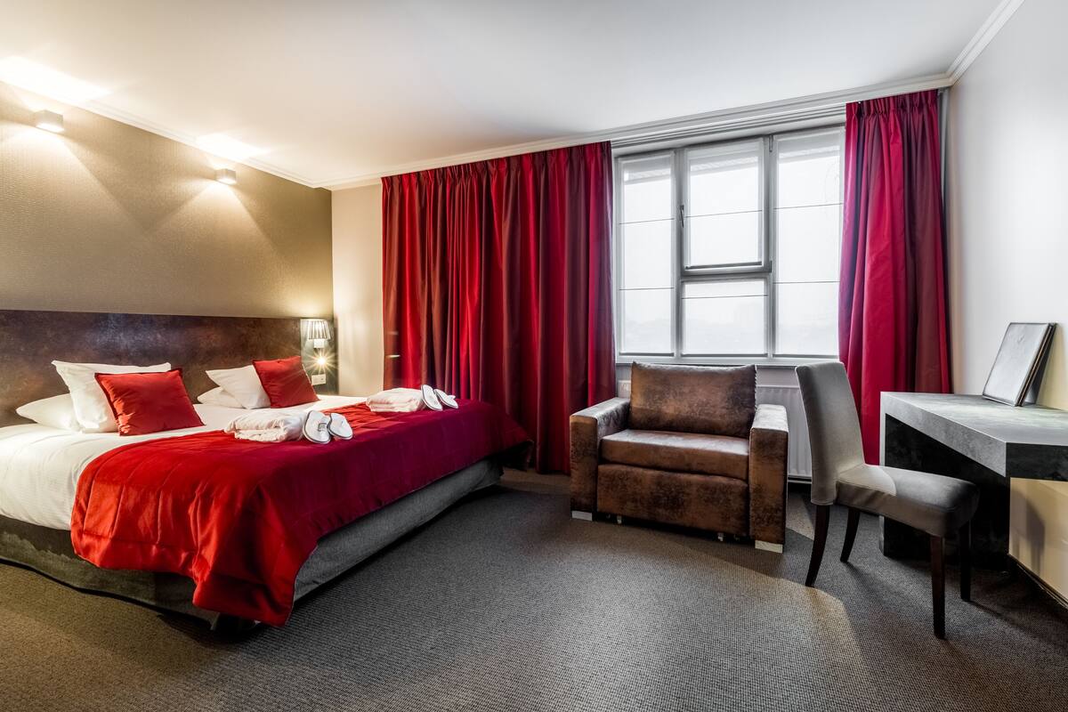 A hotel room with a bed, two chairs, a desk, and a window with curtains.