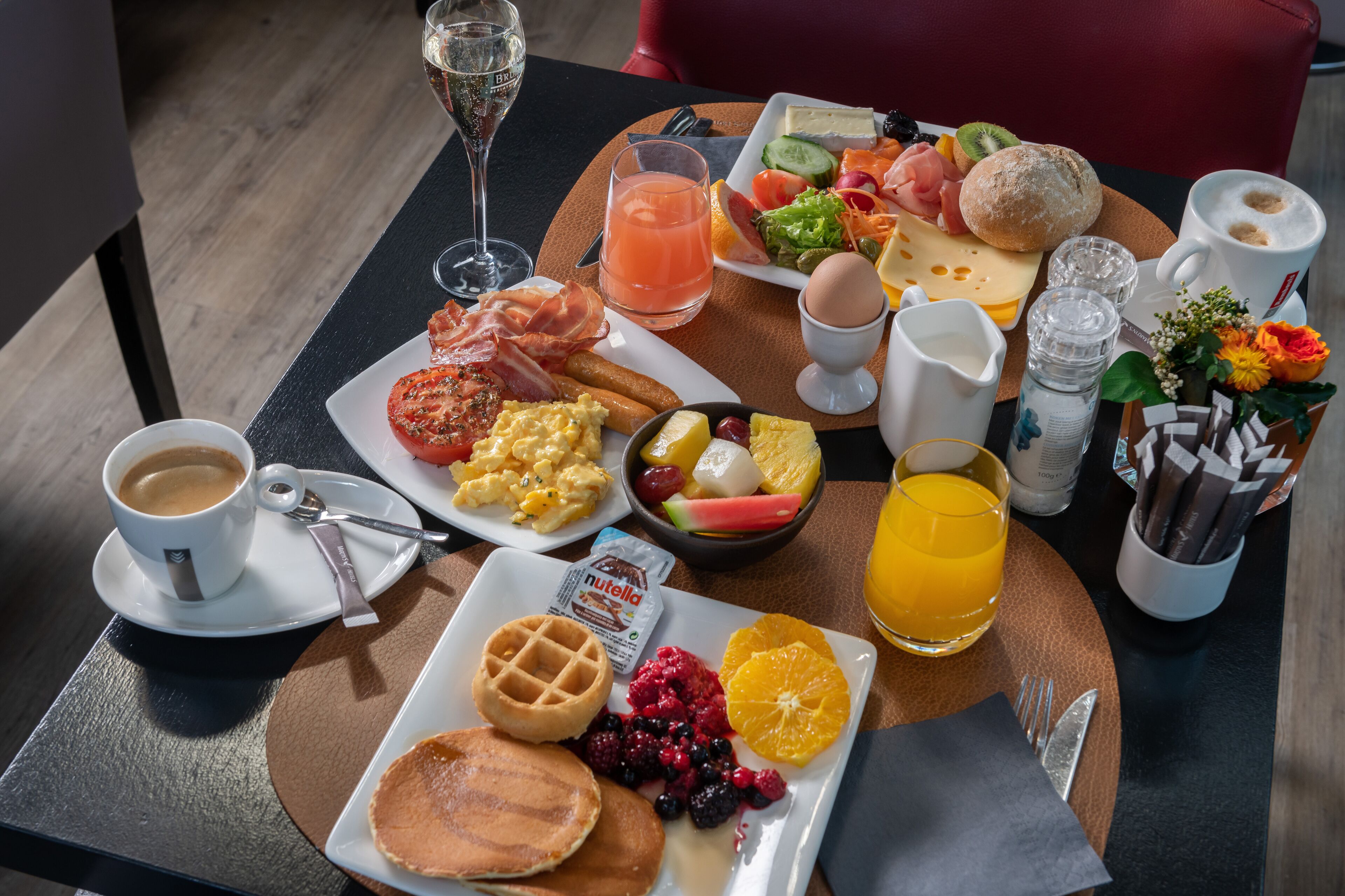 Bandeja de desayuno con panqueques, gofres, huevos revueltos y una variedad de frutas y pasteles.