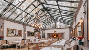 Un restaurant spacieux doté d’un haut plafond en verre, d’élégants lustres et de différents types de mobilier, notamment des tables et des chaises.