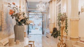 Un vaste hall d’entrée orné de colonnes richement décorées, un grand vase rempli de fleurs et un lustre.