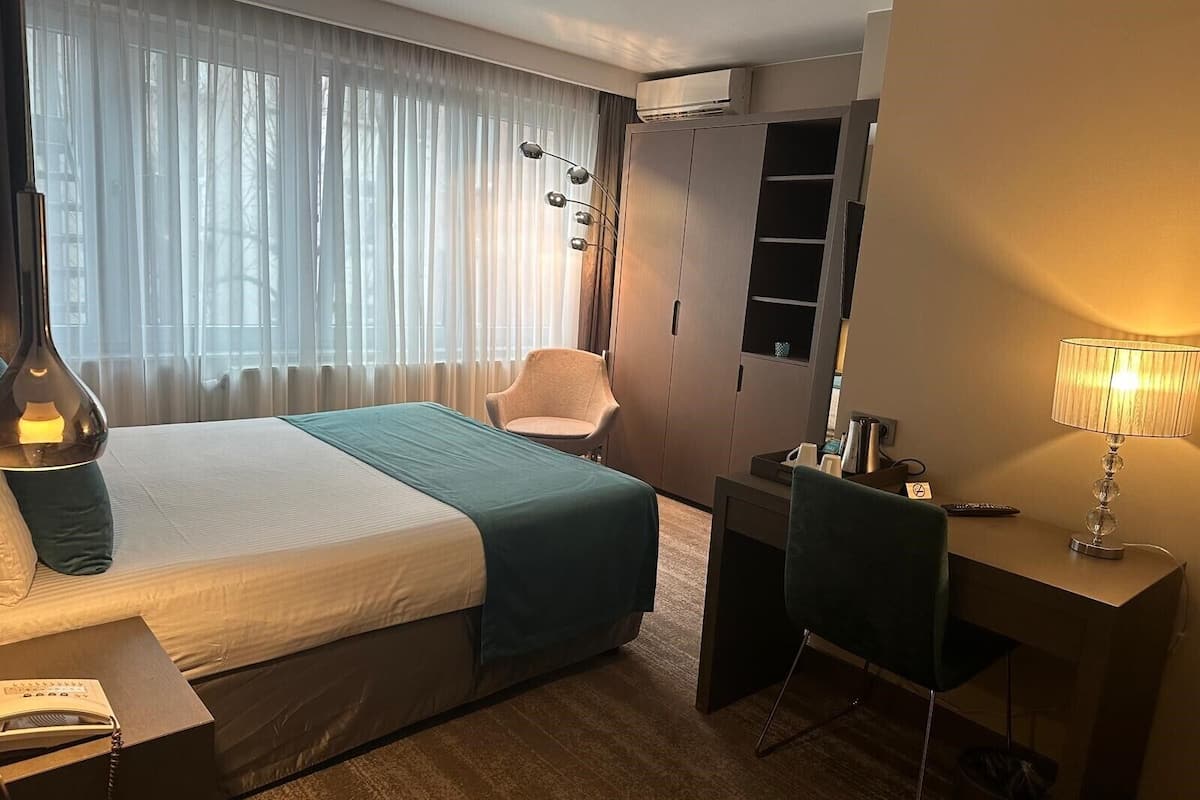 Habitación de hotel con cama, escritorio, silla, lámpara y aire acondicionado.