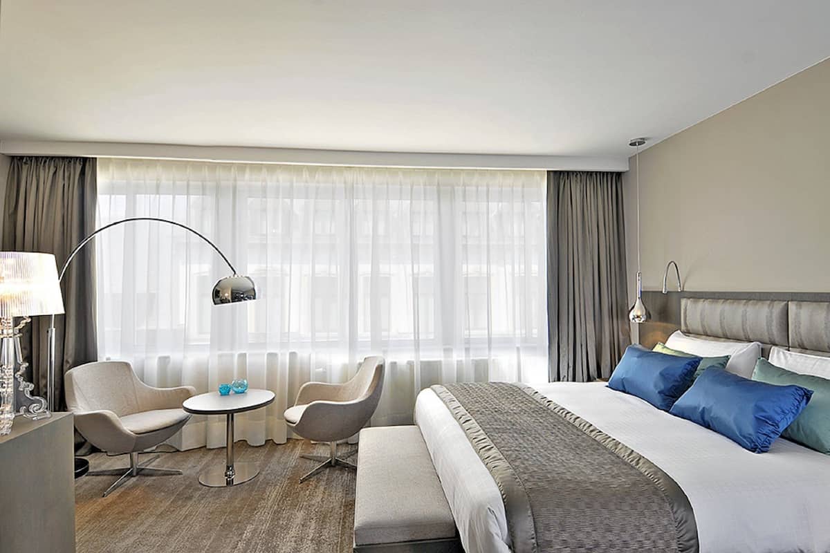 Habitación de hotel con una cama grande, dos sillones, una mesita y una lámpara de pie.