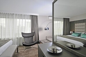 A modern hotel room with a large bed, a desk with a tray of glasses, a chair, and a mirror. - Hotel Agenda Louise (Brussels)