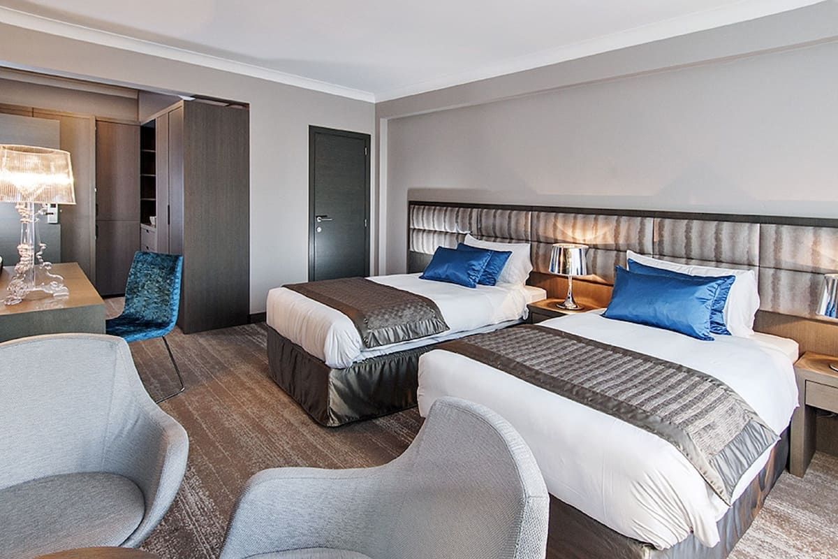 Habitación de hotel con dos camas, un escritorio, una silla y un armario.