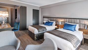 A hotel room with two beds, a desk, a chair, and a wardrobe.
