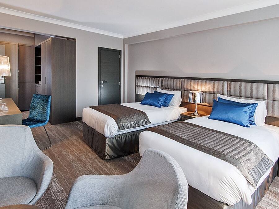 A hotel room with two beds, a desk, a chair, and a wardrobe.