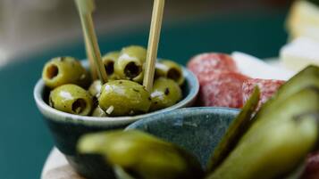 Un tazón de aceitunas con una cuchara de madera, un tazón de pepinillos y un trozo de carne sobre una tabla de madera.