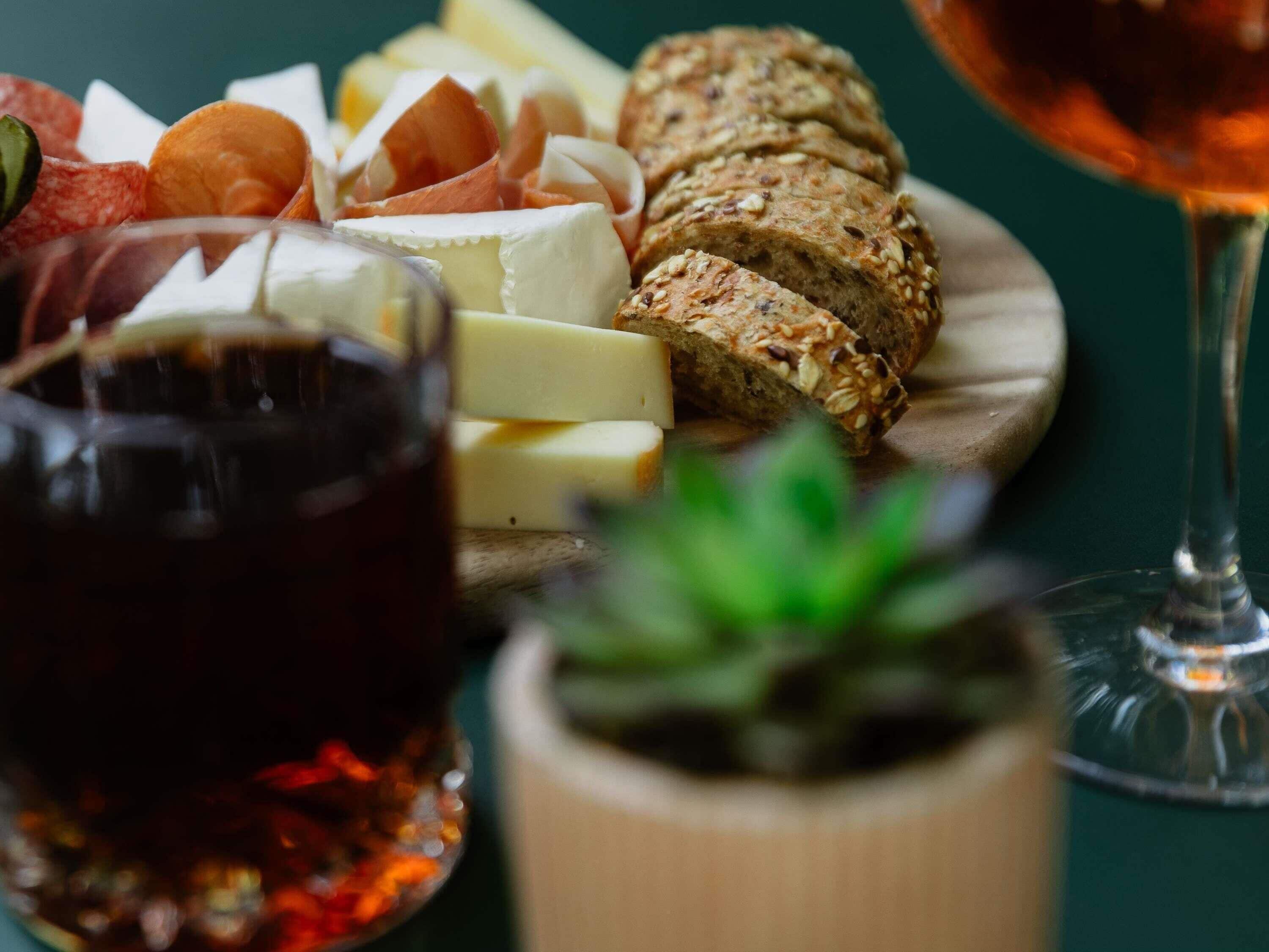 Variedad de quesos, pan y una copa de vino sobre una tabla de madera.