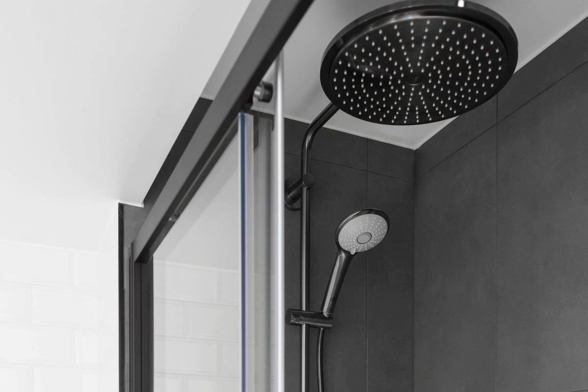 A showerhead with a circular design and a handheld attachment, mounted on a wall with a glass door.