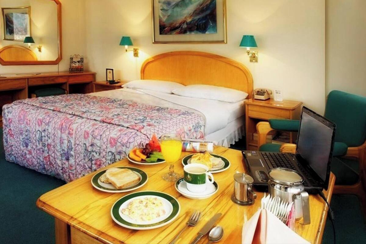 Una habitación de hotel con cama, escritorio con desayuno, una computadora portátil y una silla verde.