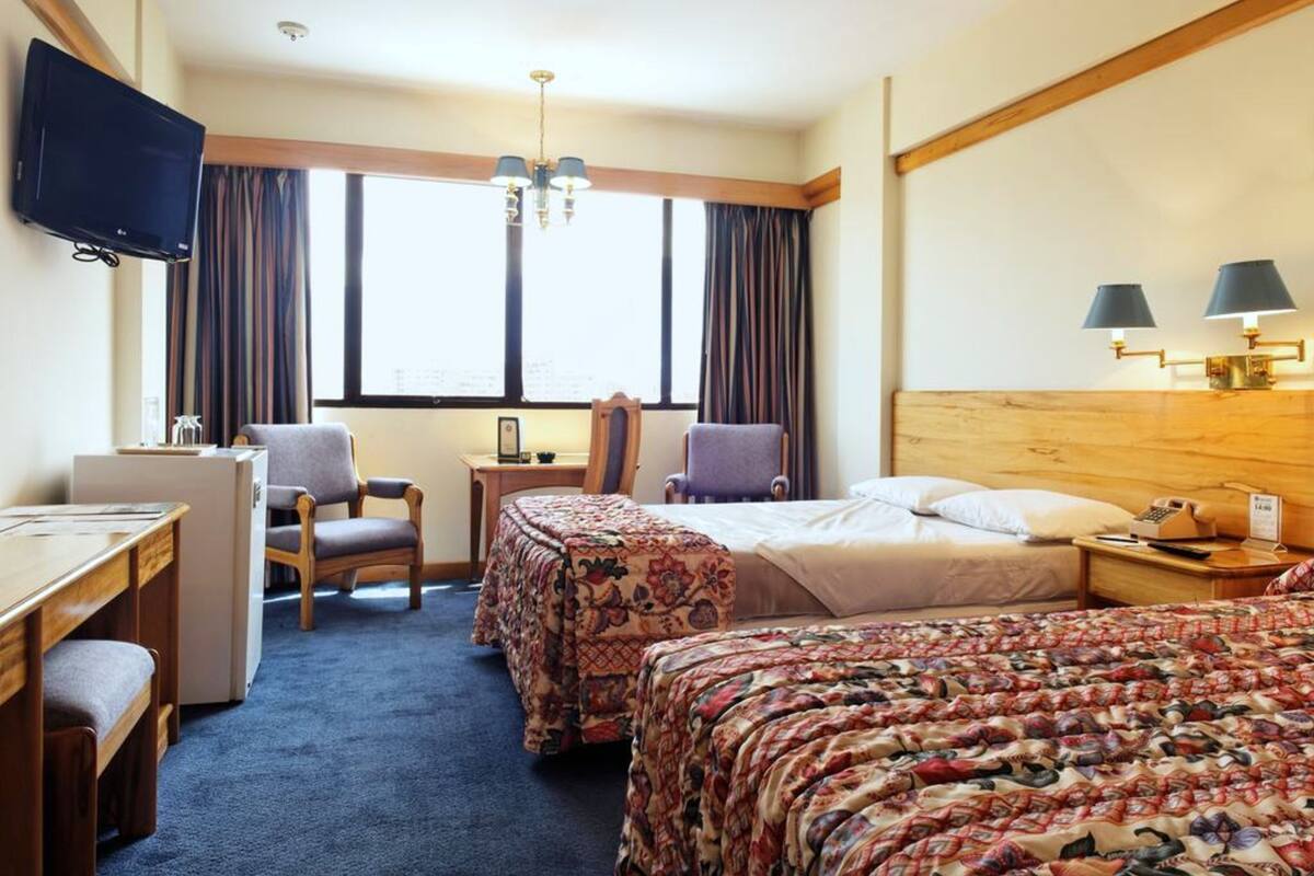 Habitación de hotel con escritorio, dos sillas, cama con ropa de cama floral, televisor y ventana con cortinas.