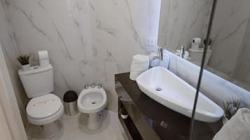 Un baño moderno con pared de mármol, encimera negra, lavamanos blanco y dos inodoros.