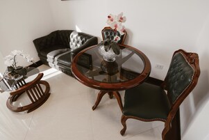 Un área de comedor con una mesa de vidrio, dos sillas, un sofá y un jarrón decorativo con flores.