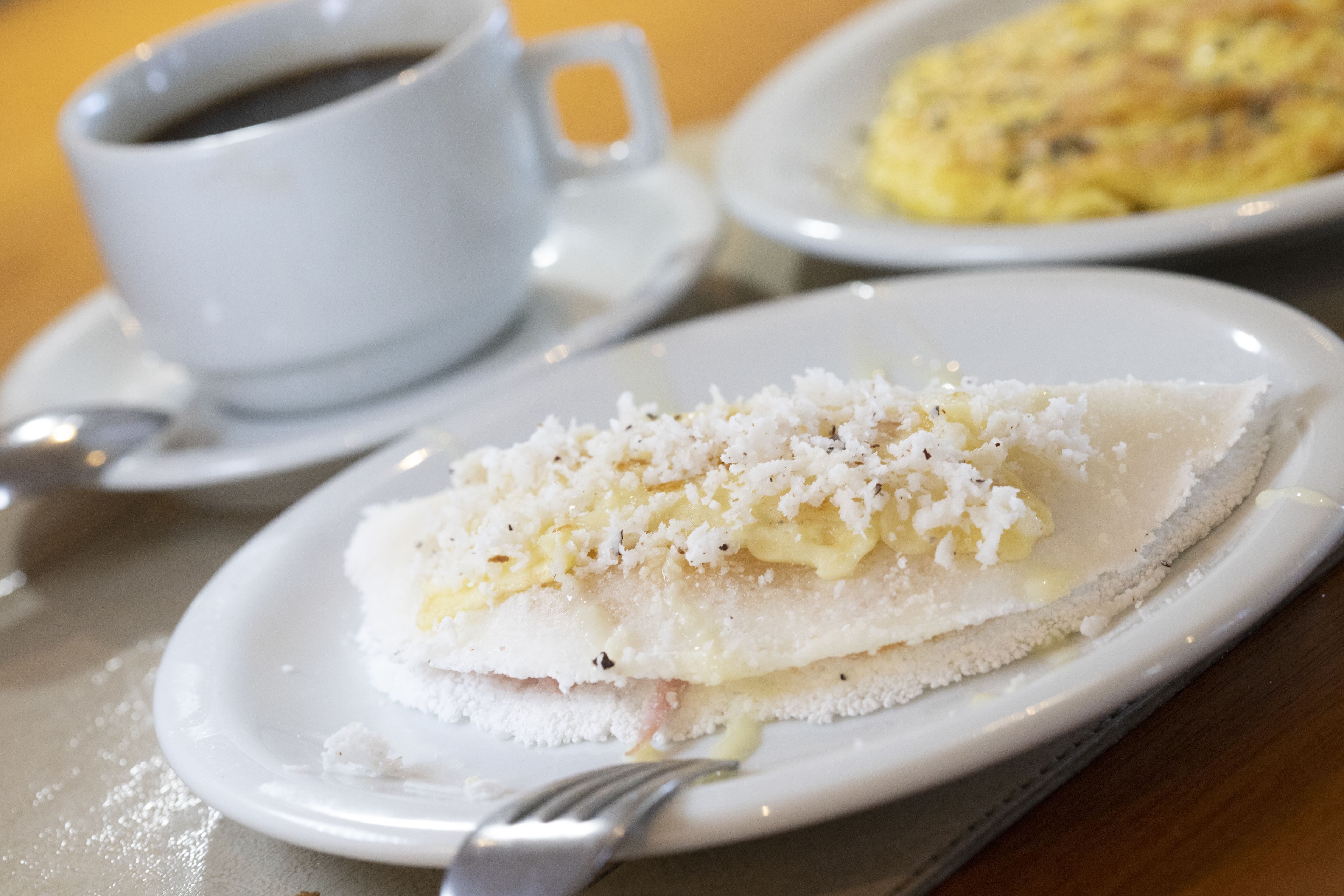A plate with a dessert topped with coconut, a cup of coffee, and a plate with scrambled eggs.