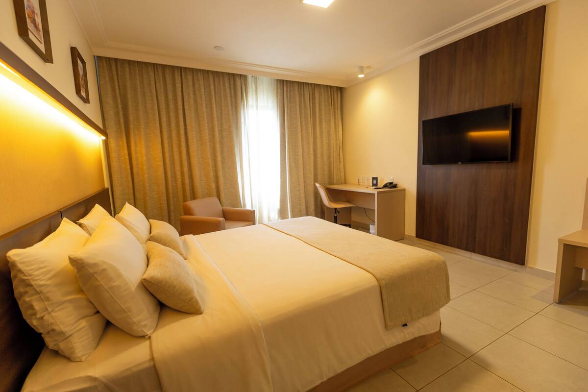 Habitación de hotel con una cama grande, un escritorio, una silla y un televisor montado en la pared.