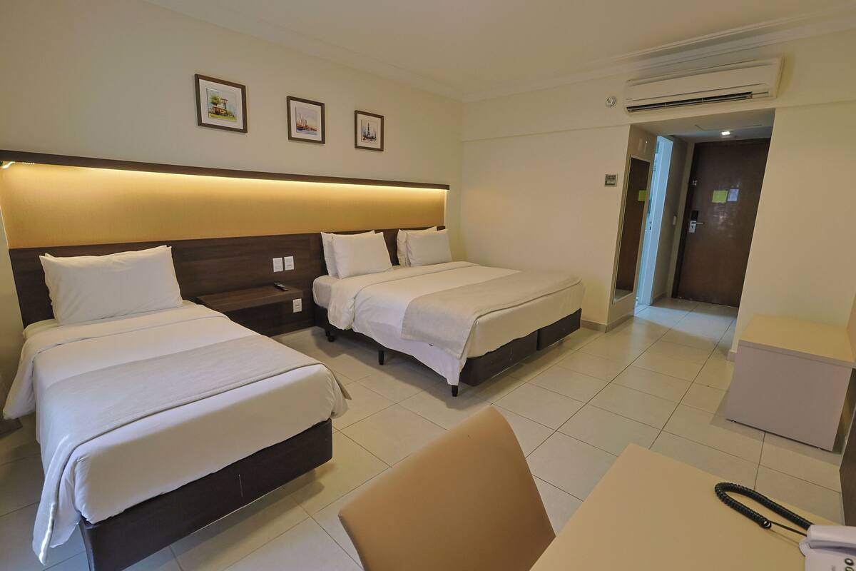 Habitación de hotel con dos camas, un escritorio y una silla. Hay cuadros en la pared y un equipo de aire acondicionado sobre las camas.