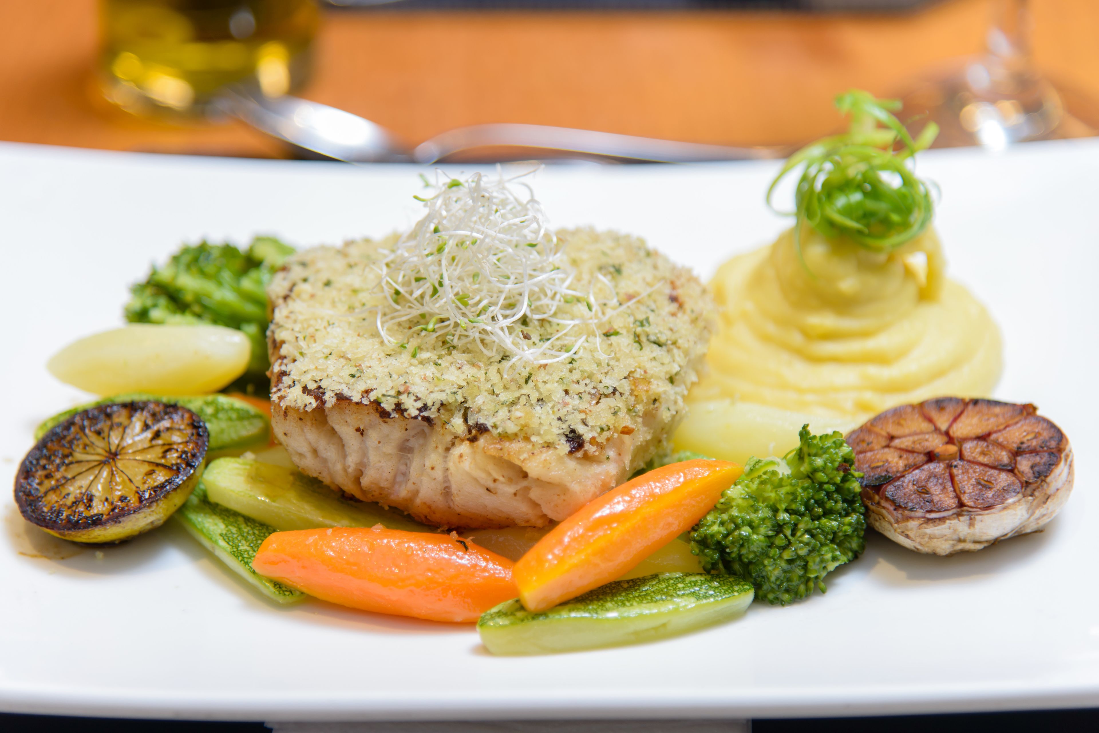 A plate of food with a piece of meat topped with breadcrumbs, accompanied by vegetables and a dollop of sauce.