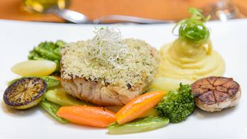 A plate of food with a piece of meat topped with breadcrumbs, accompanied by vegetables and a dollop of sauce.