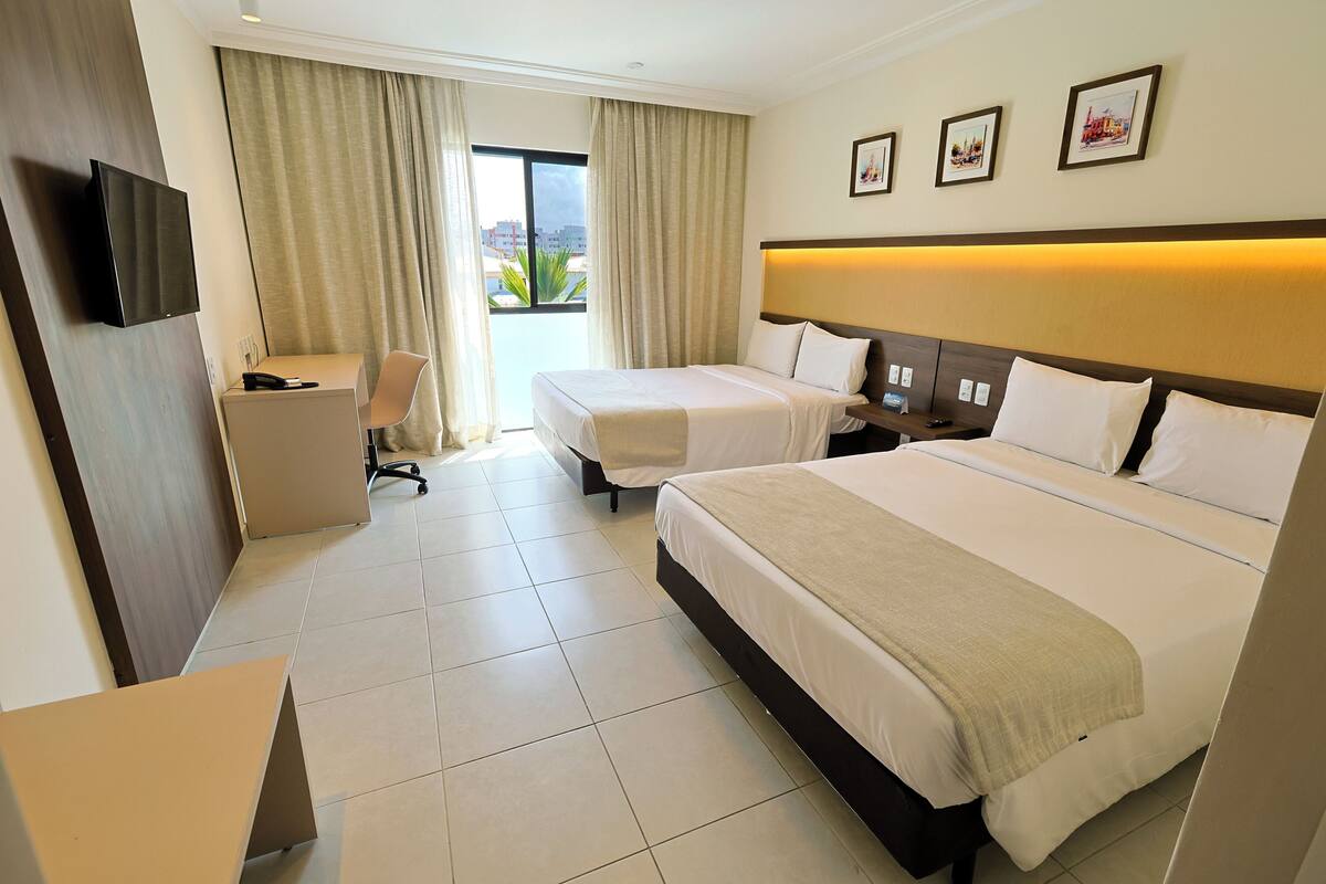 Habitación de hotel con dos camas, un escritorio, una silla, un televisor y una ventana con cortinas.