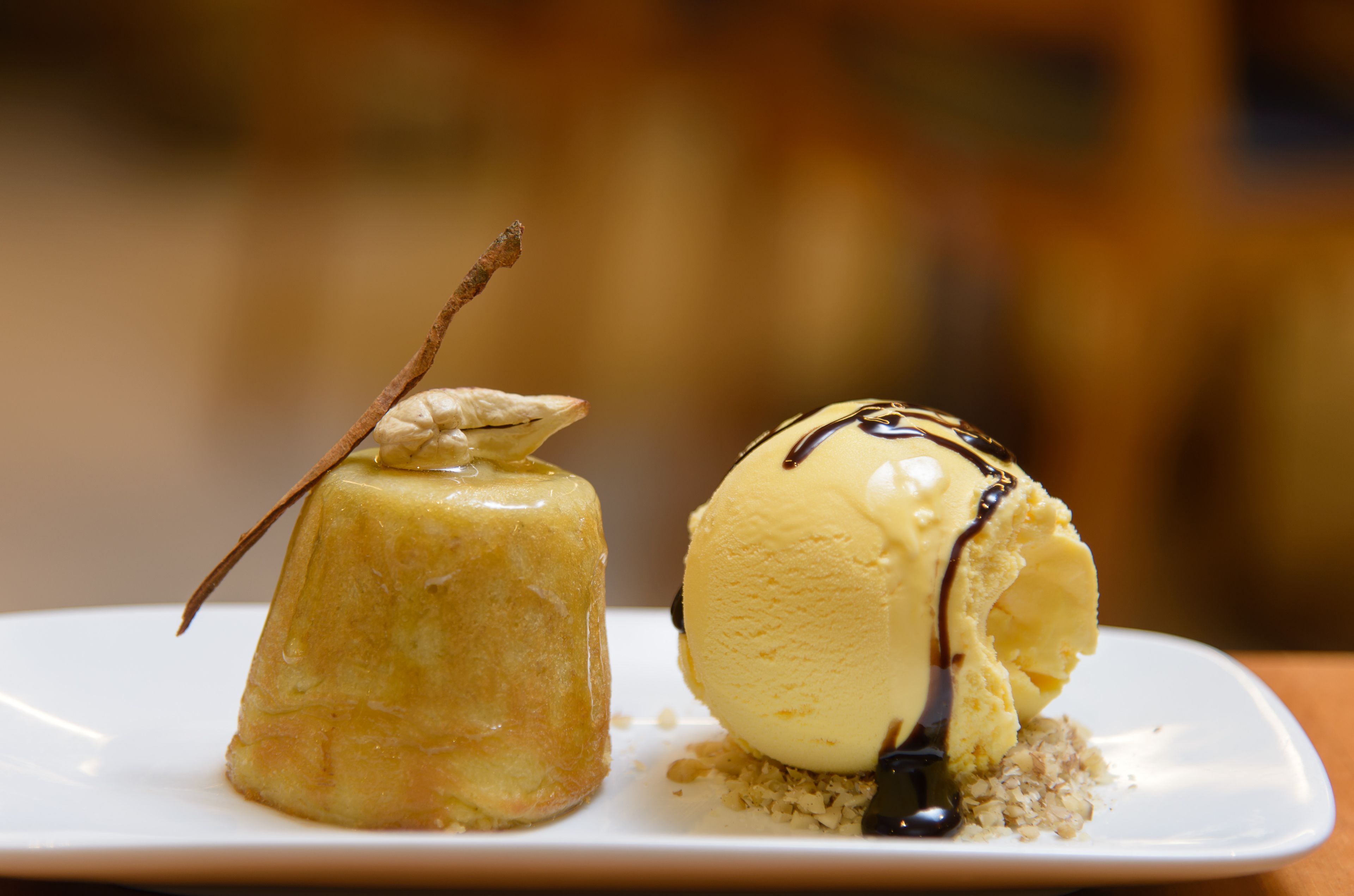 A dessert plate with a caramel flan and a scoop of vanilla ice cream drizzled with chocolate sauce.