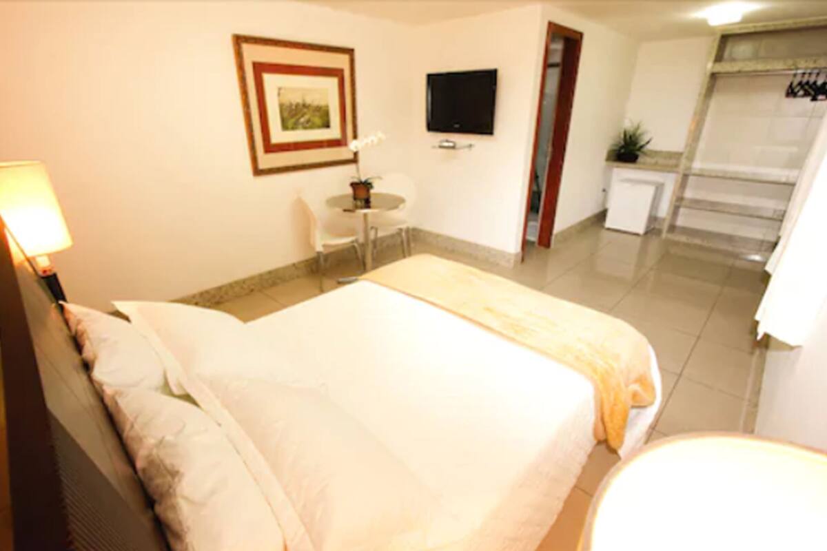Une chambre d’hôtel équipée d’un lit, d’un bureau, d’une chaise, d’une télévision et d’une petite kitchenette.