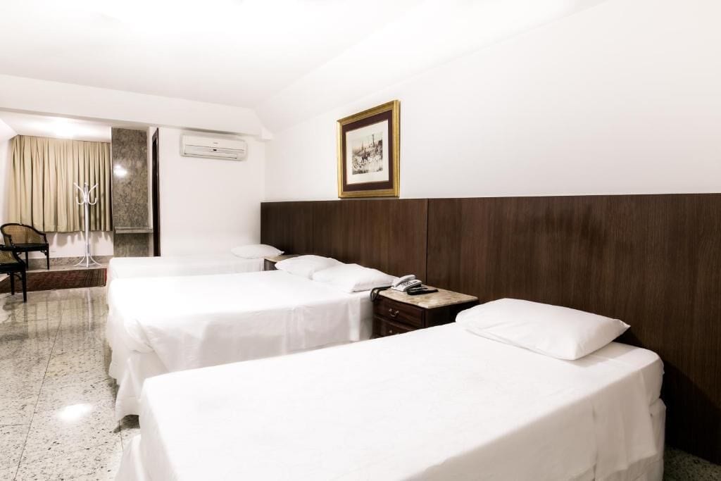 A hotel room with two single beds, a wooden headboard, a bedside table with a phone, a chair, and a coat rack.