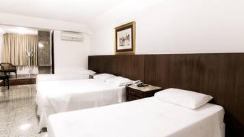 A hotel room with two single beds, a wooden headboard, a bedside table with a phone, a chair, and a coat rack.