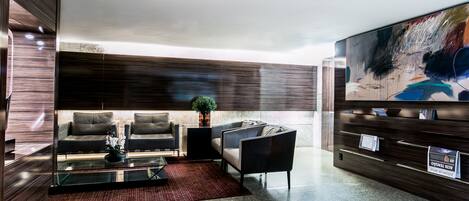 Un lobby moderno con paneles de madera oscura, sofás de cuero, una mesa de centro de vidrio y un gran cuadro abstracto en la pared.