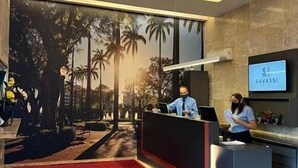 A reception area with a red carpet, a large window with a tropical view, and a sign that reads "SAVASSI". - Savassi Hotel (Belo Horizonte)
