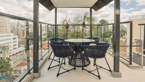 A balcony with a round table and chairs, overlooking a cityscape with buildings and palm trees. - Savassi Hotel (Belo Horizonte)