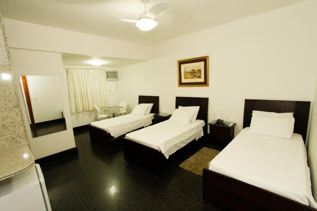 A hotel room with two single beds, a ceiling fan, a framed picture on the wall, and a small table with a chair.