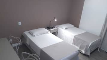 Quarto pequeno e limpo, com duas camas de solteiro, uma escrivaninha e uma cadeira.