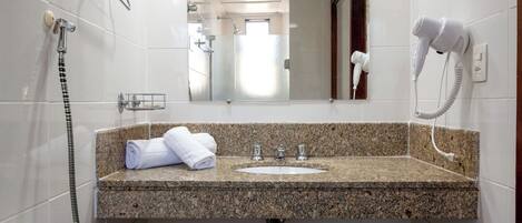 Un baño con encimera de granito, un lavabo, un espejo, un perchero para toallas, un secador de pelo y una ducha.