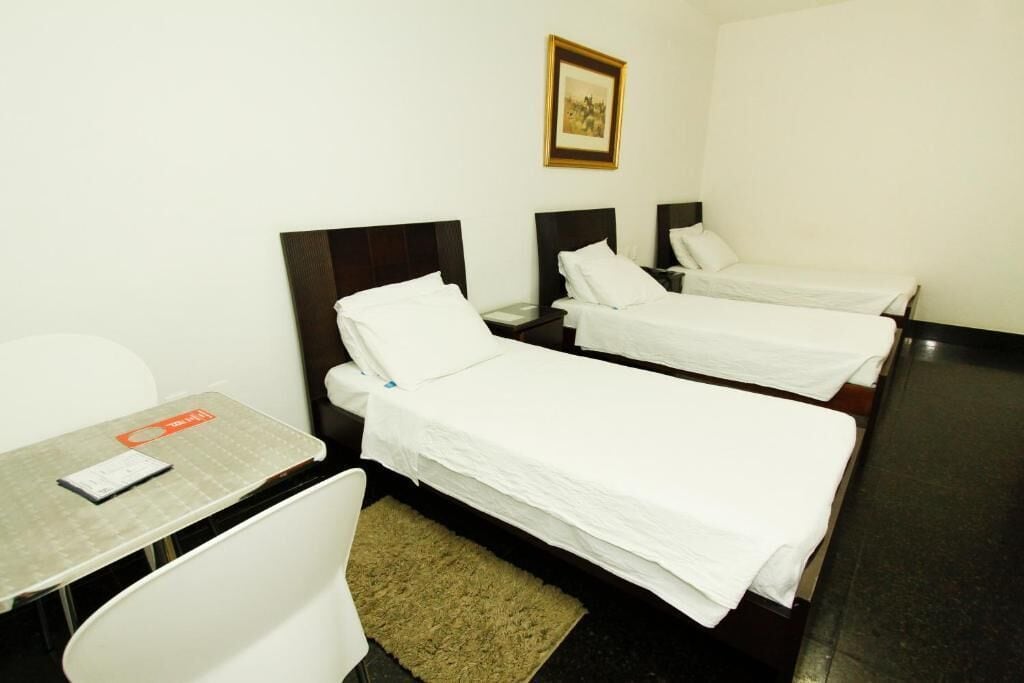 Quarto de hotel com duas camas de solteiro, uma mesinha com uma cadeira e um quadro na parede.