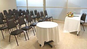 Une salle de conférence avec des rangées de chaises et une table ronde recouverte d’une nappe blanche.