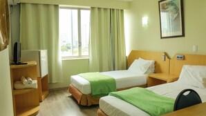Une chambre d’hôtel avec deux lits, un bureau, une chaise, une télévision et une fenêtre avec des rideaux.