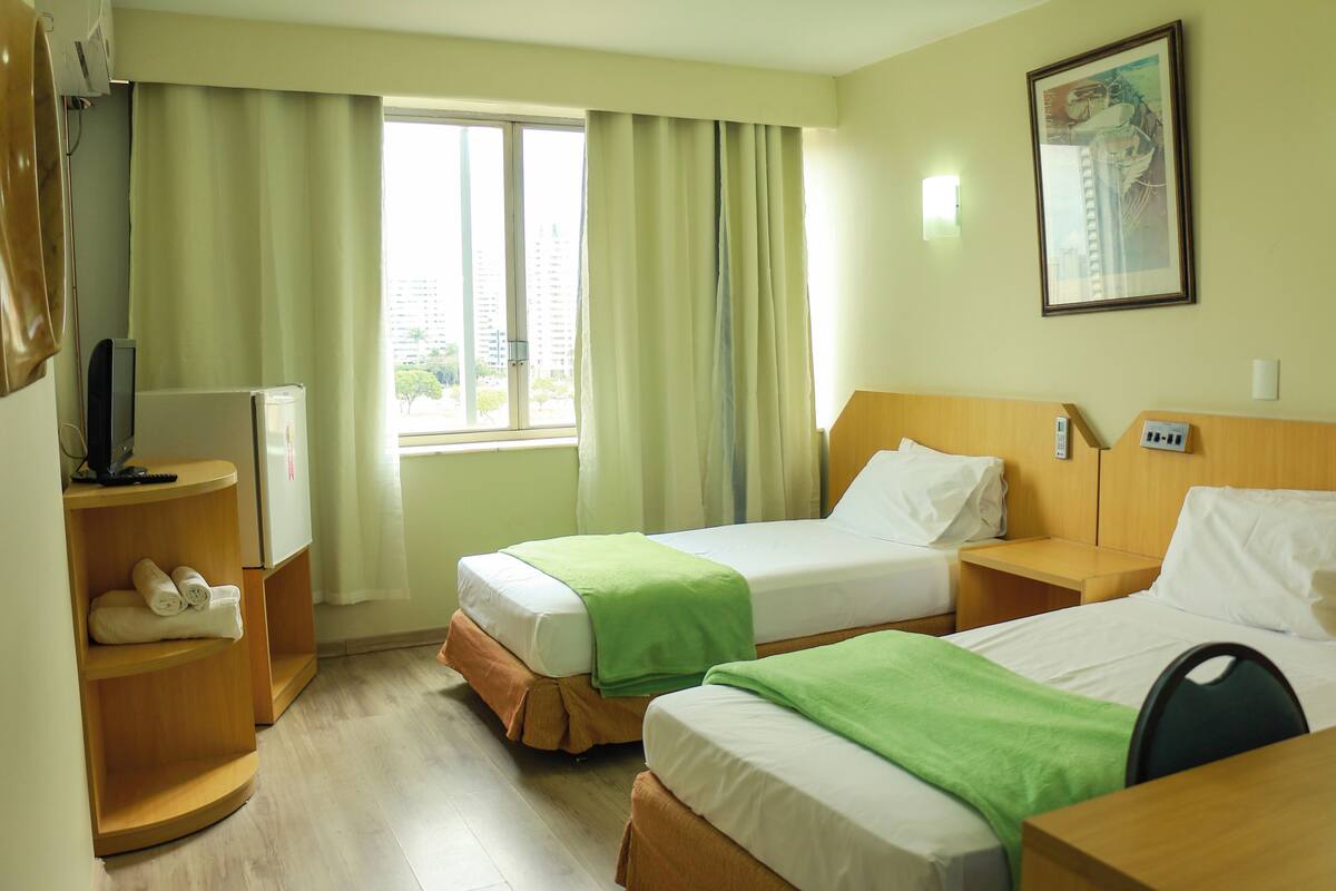 A hotel room with two beds, a desk, a chair, a TV, and a window with curtains.