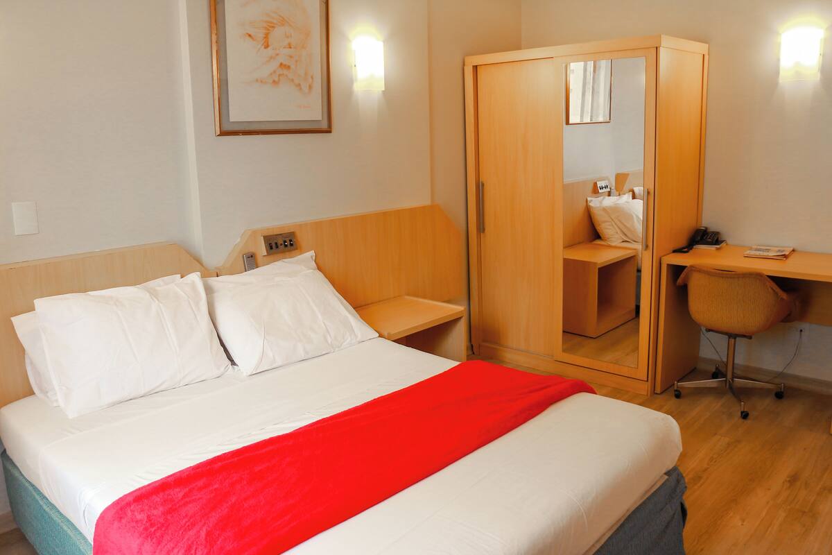 A hotel room with a bed, a desk, a chair, and a wardrobe.