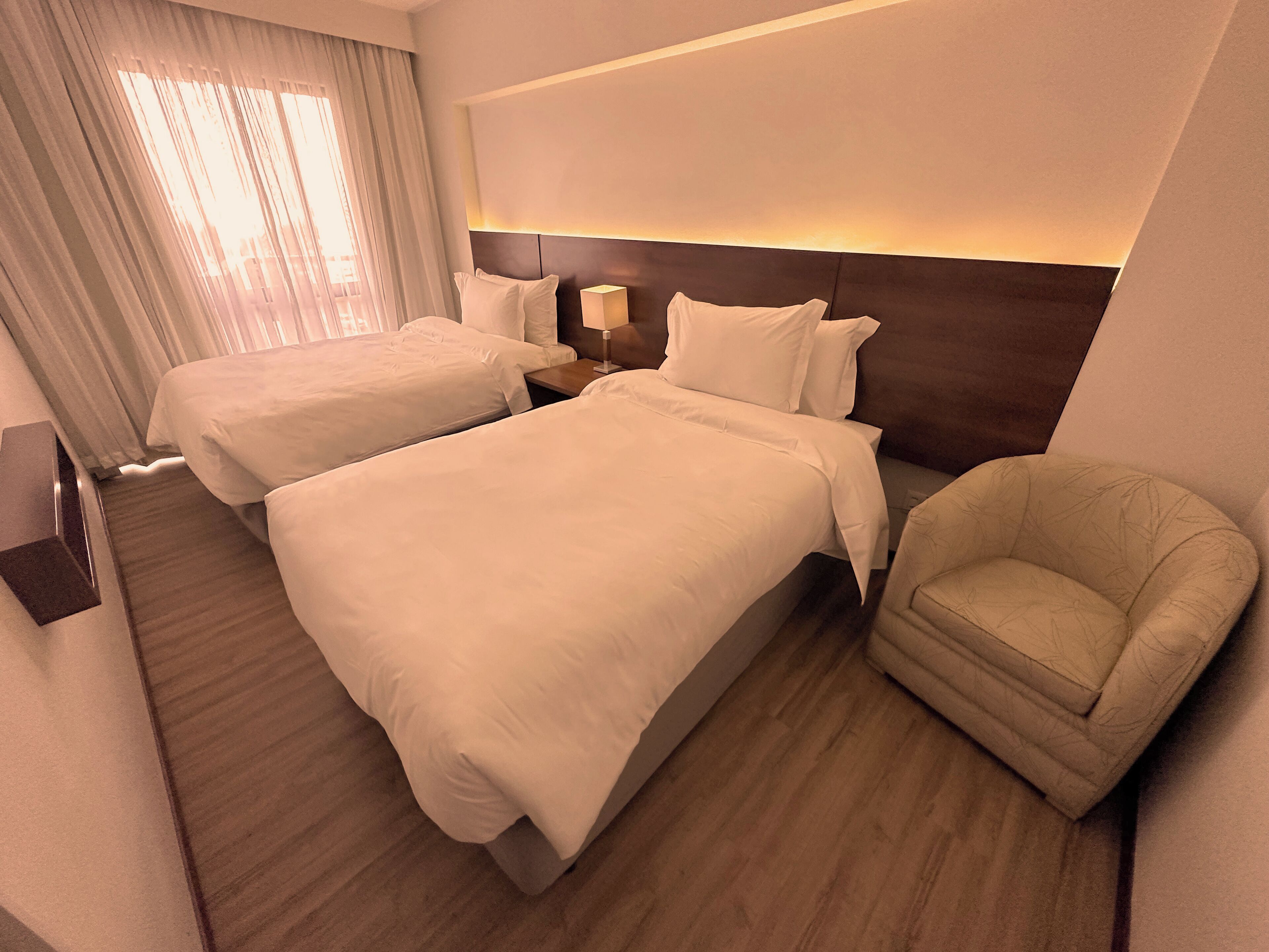 Habitación de hotel con dos camas, una silla, una mesita de noche y una lámpara.