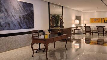 Un vestíbulo de hotel moderno con un gran cuadro abstracto, una recepción, asientos cómodos y un espejo grande que refleja el espacio.
