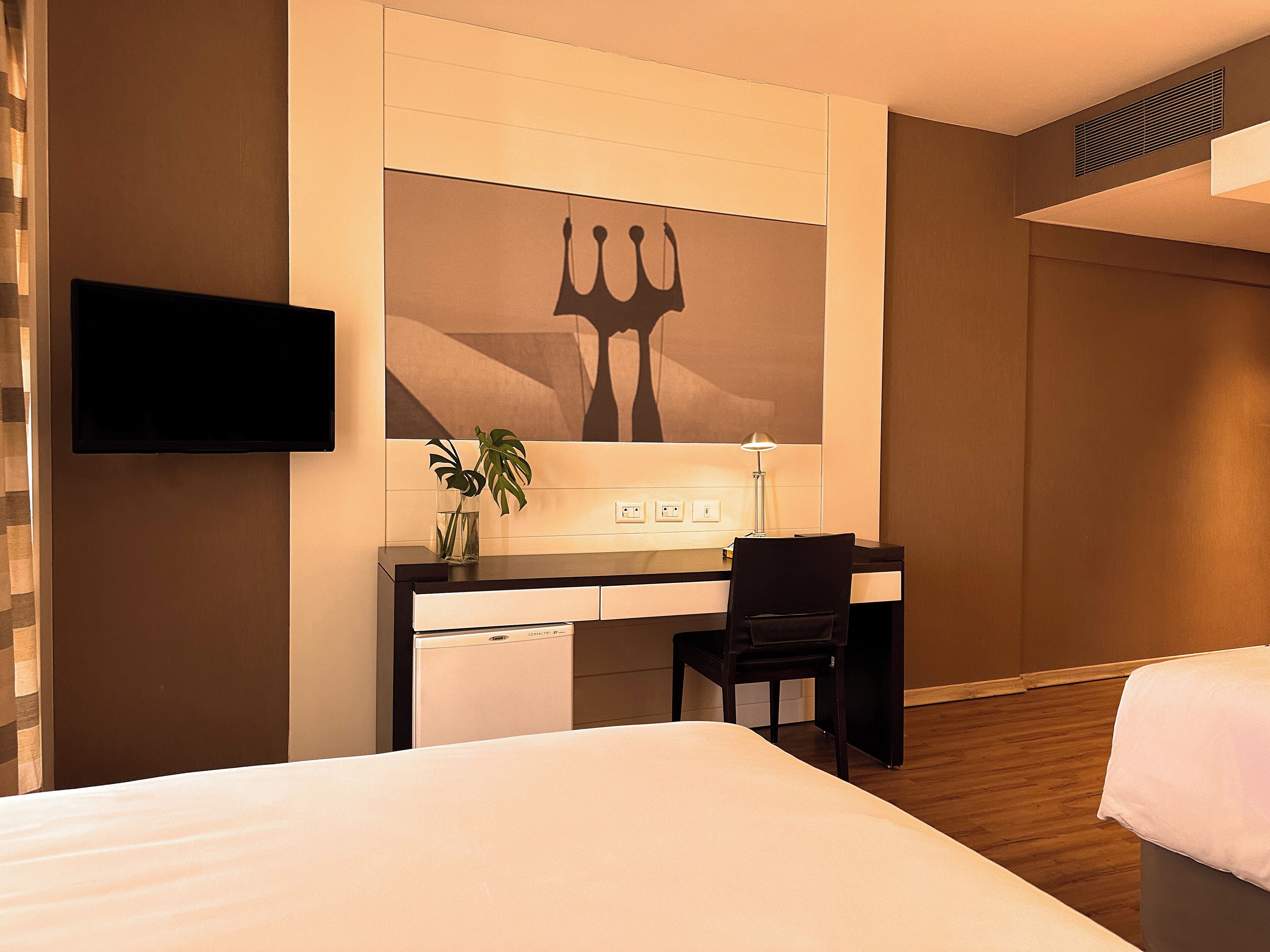 Una habitación de hotel con cama, escritorio, silla, televisor y una obra de arte colgada en la pared.
