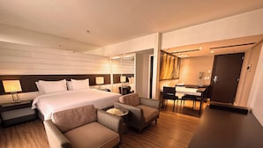 Une chambre d’hôtel moderne dotée d’un grand lit, d’un coin salon avec deux fauteuils, d’une petite table, d’un bureau avec une chaise et d’un miroir.