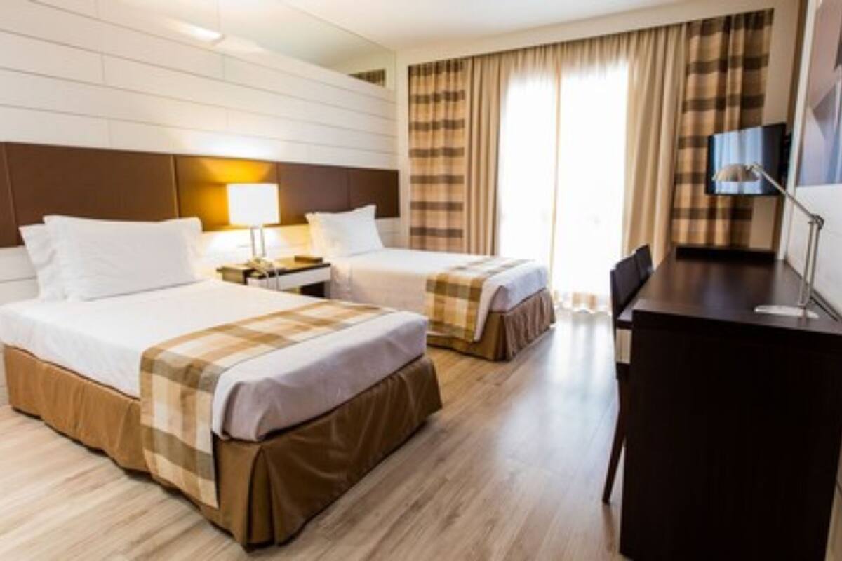 Habitación de hotel con dos camas, un escritorio, un televisor y una ventana con cortinas.